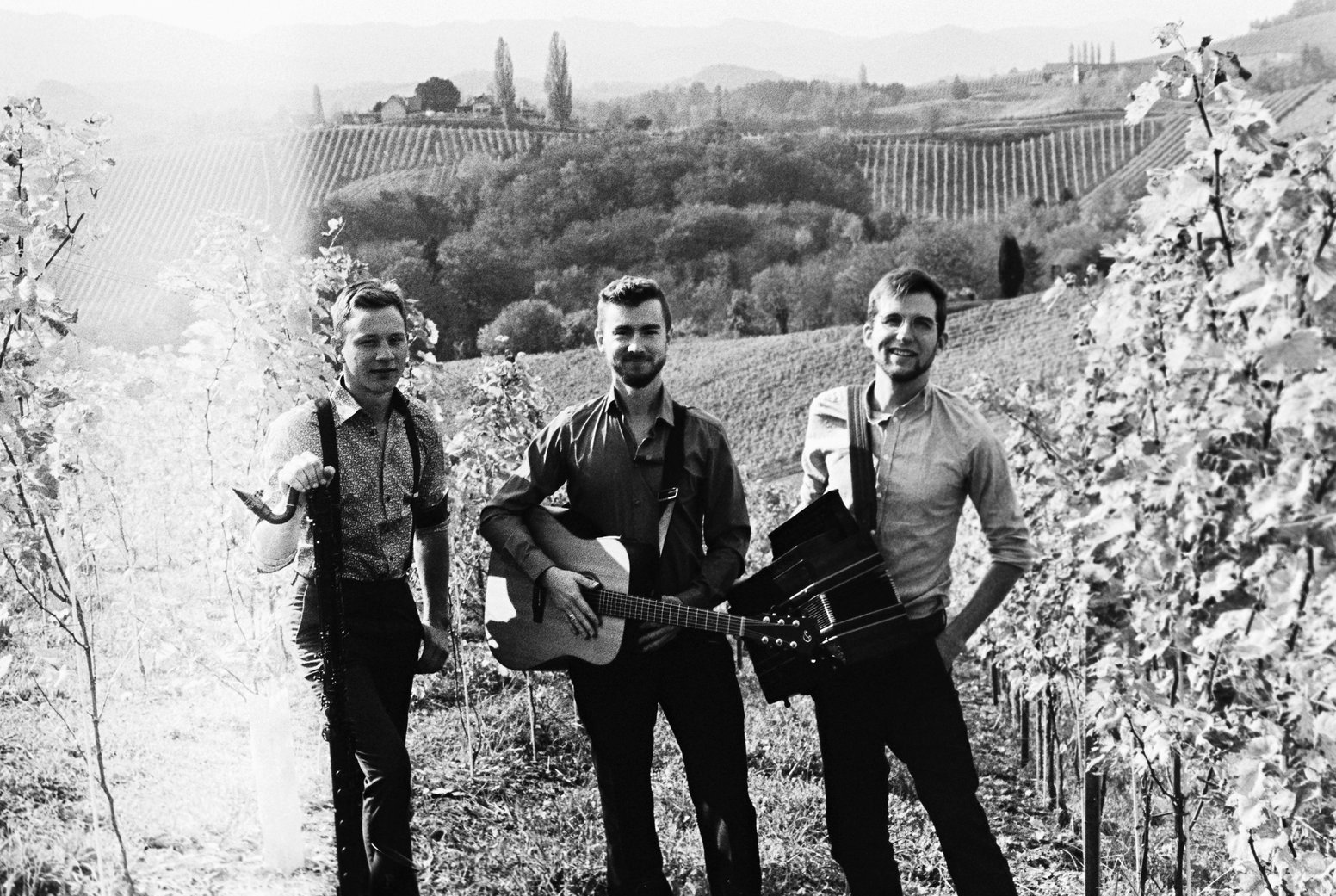 Die Band Sturm & Klang im Weinberg: drei Musiker in Hemd und Hosenträgern, in der Mitte mit Gitarre, rechts mit Steirischer Harmonika, Schwarzweiß-Foto von Johanna Seitinger.