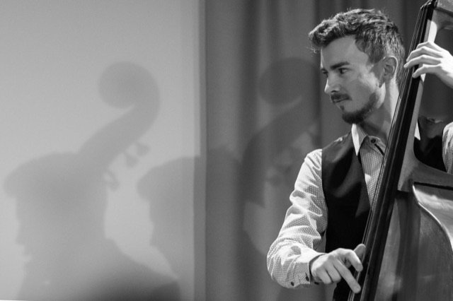 Max Ganster am Kontrabass im Profil, sein Schatten an der hellen Wand, Schwarzweiß-Foto.